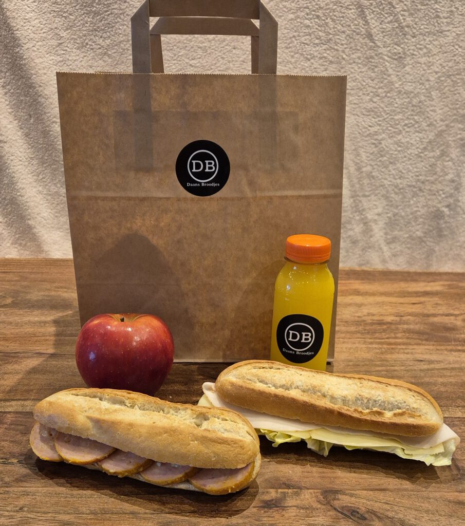 Een lunchpakket/tas met 2 belegde baguettes, jus d'orange en een appel